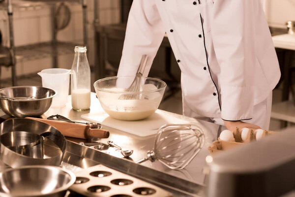 partial view of confectioner standing at counter with raw dough in bowl