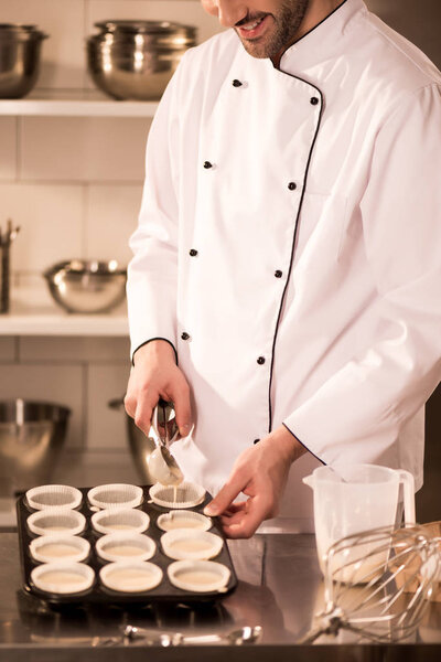 cropped shot of confectioner pouring dough into baking forms