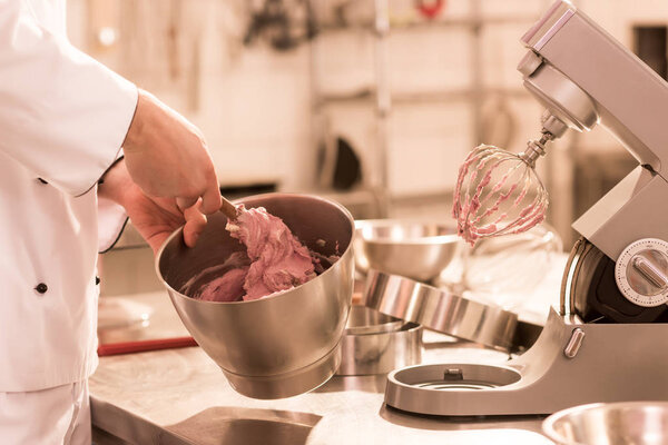 partial view of confectioner making cream for dessert in restaurant kitchen