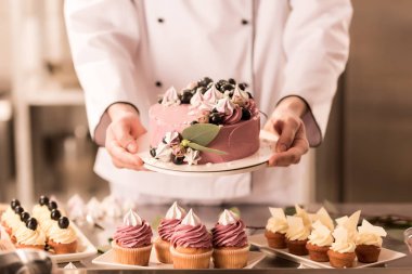 partial view of confectioner holding cake in hands in restaurant kitchen clipart