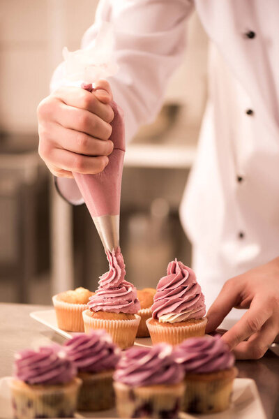cropped shot of confectioner putting cream on cupcakes