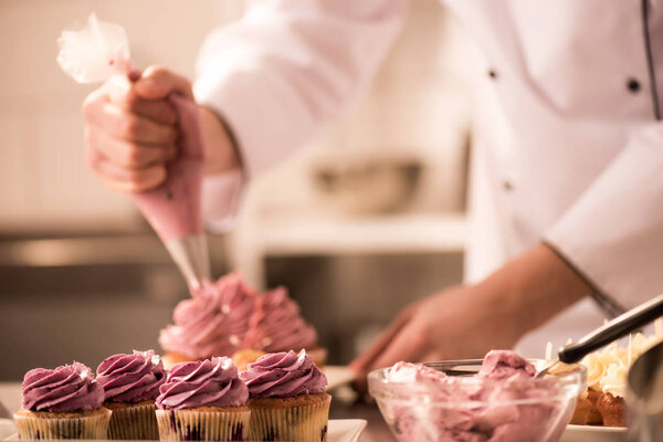 cropped shot of confectioner putting cream on cupcakes