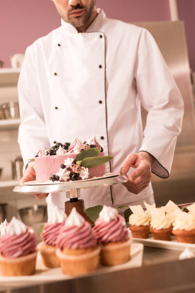 partial view of confectioner holding cake in restaurant kitchen