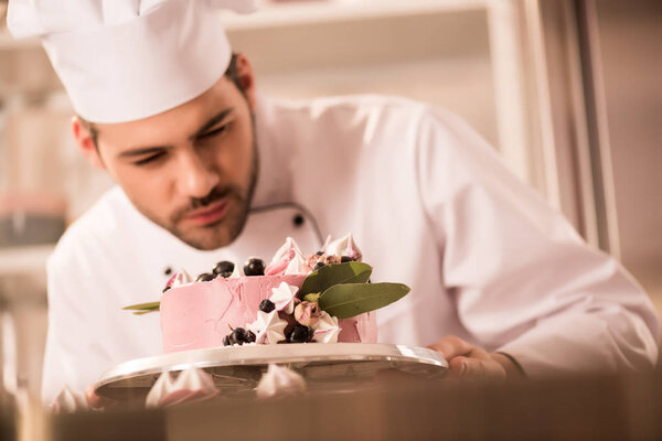 selective focus of confectioner looking at cake in hands in restaurant kitchen