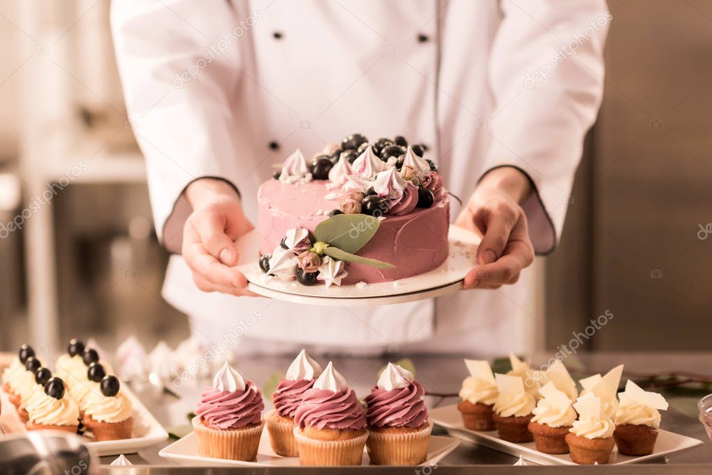 partial view of confectioner holding cake in hands in restaurant kitchen