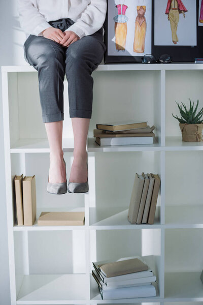 cropped shot of stylish woman sitting on bookshelves