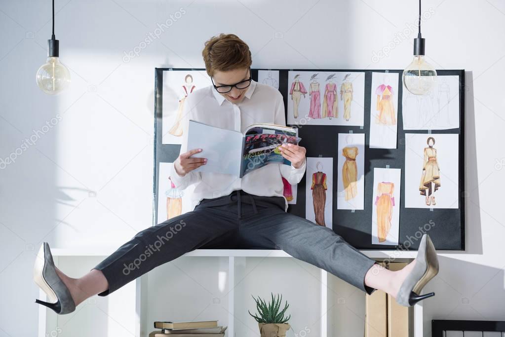fashion designer sitting on bookshelves and reading magazine