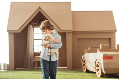little kid holding his adorable labrador puppy in front of cardboard house isolated on white clipart