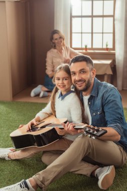 mutlu baba ve kız içinde oturan annesi ile karton evin önünde çimenlerin üzerinde gitar çalmak
