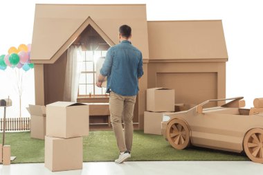 rear view of man with boxes moving into new cardboard house isolated on white clipart