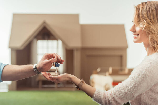 обрезанный снимок агента по недвижимости передающий ключ счастливой женщине перед картонным домом
