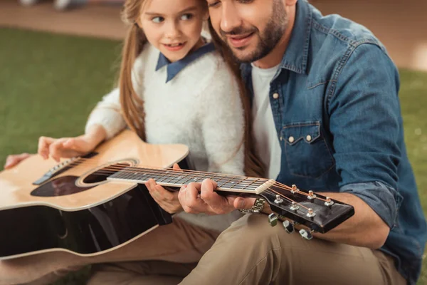 handsome father and daughter playing guitar while sitting on grass