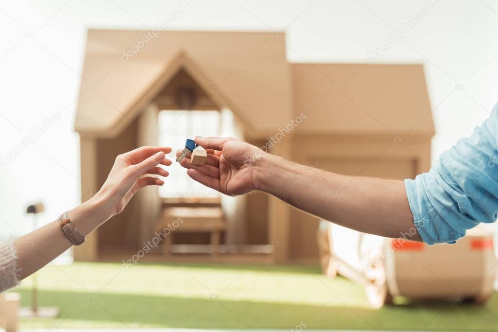 cropped shot of real estate agent passing key to client in front of cardboard house