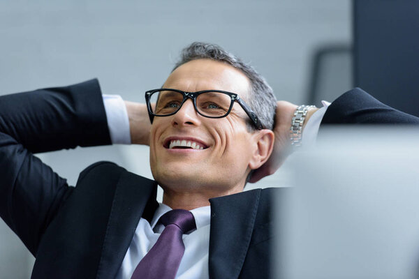 portrait of cheerful businessman in eyeglasses with hands behind head