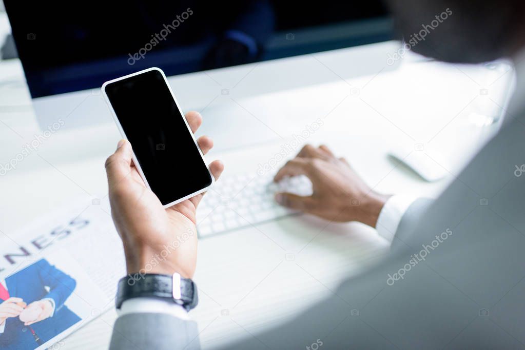 partial view of businessman using smartphone at workplace 