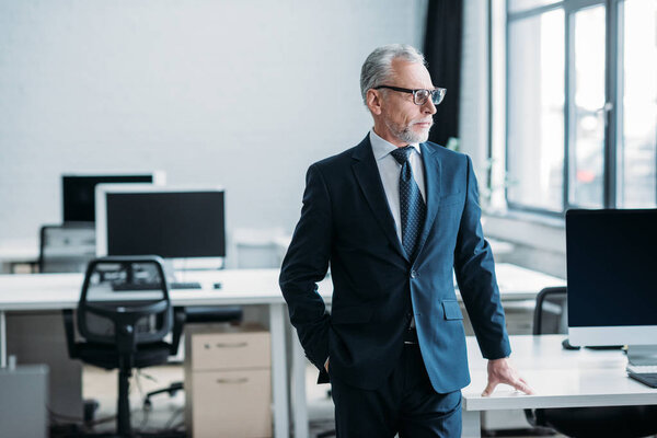 senior businessman in eyeglasses standing at workplace in office 