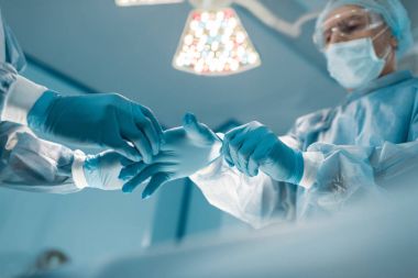 cropped image of nurse helping surgeon wear medical gloves clipart