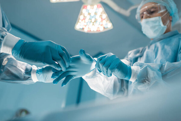 обрезанный образ медсестры, помогающей хирургу носить медицинские перчатки
