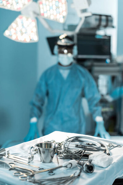 хирург смотрит на камеру в операционной с инструментами на переднем плане
