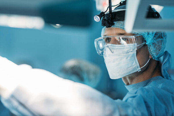 красивый хирург в медицинской маске и очках, отворачивающийся
