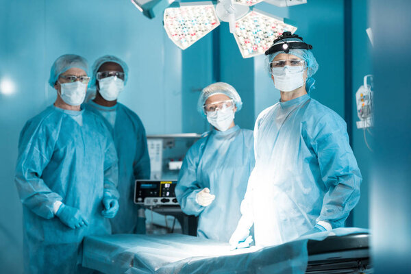 четыре мультикультурных врача смотрят в операционную на камеру
