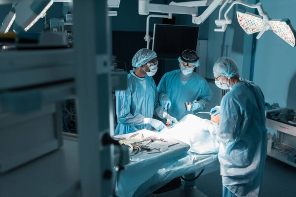 три мультикультурных хирурга и пациент в операционной
