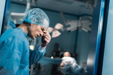 yorgun doktor ameliyat odasında burun köprüsü dokunmadan yan görünüm