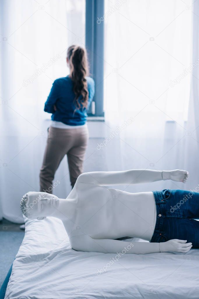 back view of woman standing at window and layman doll lying on bed, loneliness concept