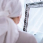 Baksidan på sjuk kvinna i halsduk stående nära spegel, cancer koncept