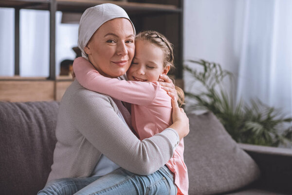 sick mature woman in kerchief hugging cute little granddaughter, cancer concept