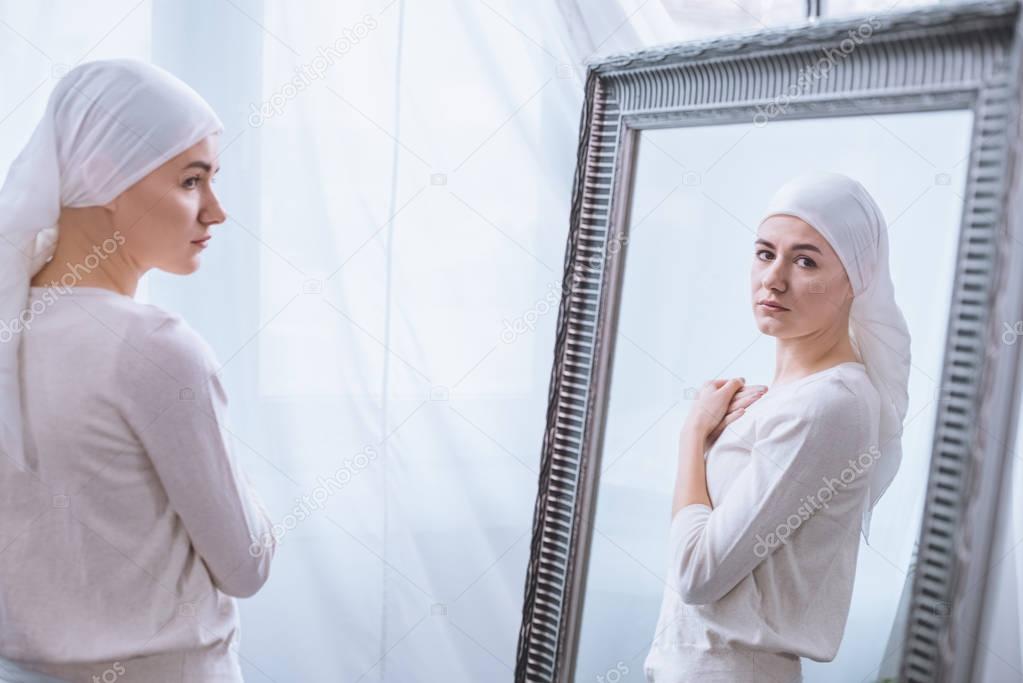 young sick woman in kerchief looking at mirror, cancer concept