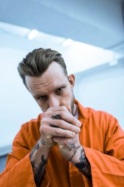 tattooed prisoner covering mouth with hands and looking at camera clipart