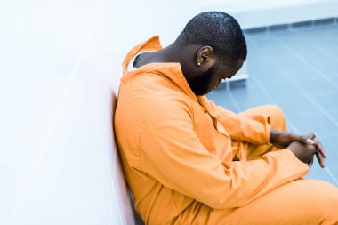 hapishane hücresinde bankta oturan üzgün Afro-Amerikan mahkum