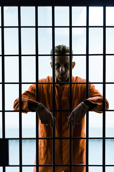 prisoner putting hands between prison bars and looking at camera