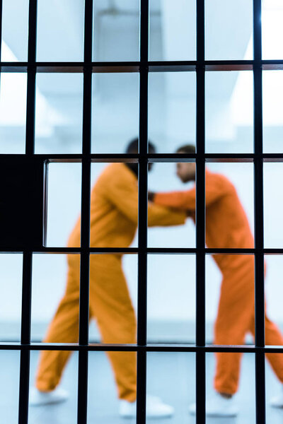 взгляд сбоку на многоэтнических заключенных, угрожающих друг другу за тюремной решеткой
