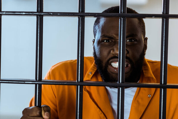 angry african american prisoner holding prison bars