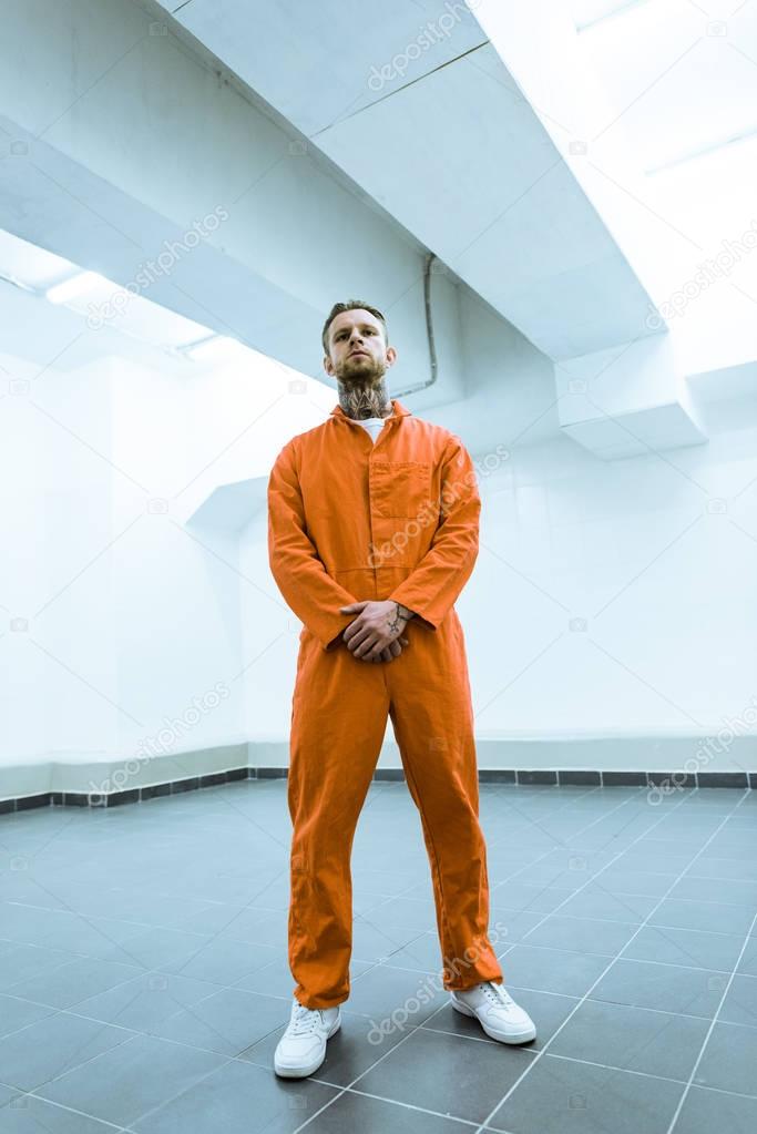 bottom view of tattooed prisoner standing in prison cell