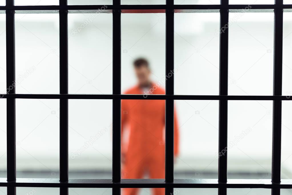 prisoner in prison cell with metallic bars on foreground 