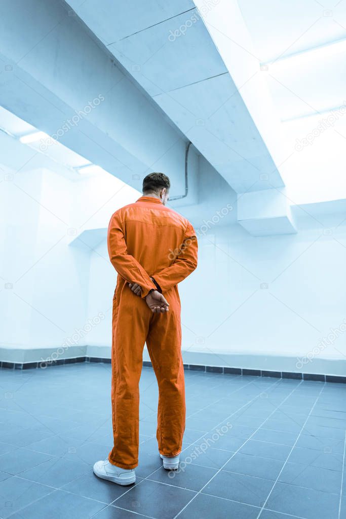 rear view of prisoner in orange uniform standing in prison cell