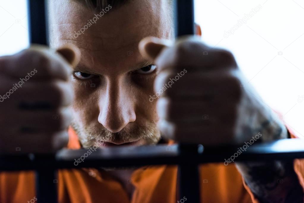 aggressive prisoner holding prison bars and looking at camera