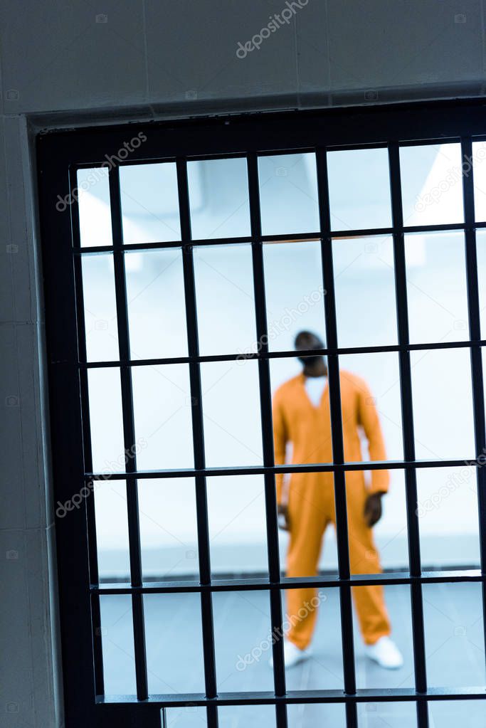 african american prisoner standing behind prison bars
