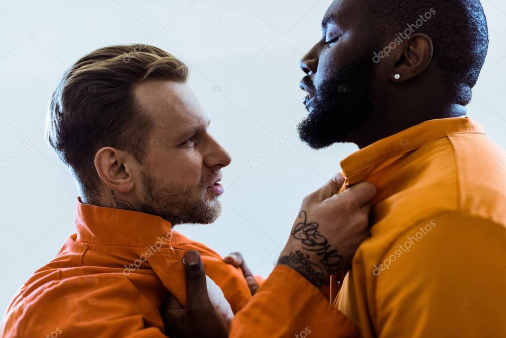 side view of multiethnic prisoners threatening each other and holding collars