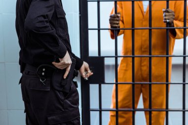 cropped image of prison guard putting hand on gun near prison bars clipart