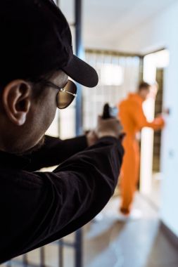 prison guard aiming gun at prisoner  clipart