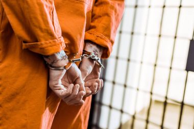 cropped image of tattooed prisoner standing in handcuffs in corridor clipart