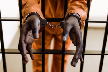cropped image of african american prisoner in handcuffs behind prison bars  clipart