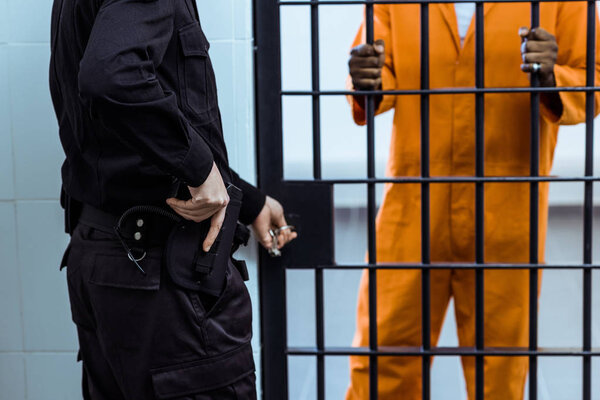 cropped image of prison guard putting hand on gun near prison bars