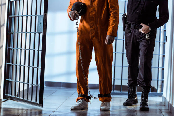 обрезанное изображение тюремного офицера ведущего заключенного, несущего вес привязанный к ноге
