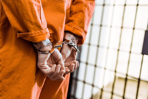 обрезанное изображение татуированного заключенного, стоящего в наручниках в коридоре
