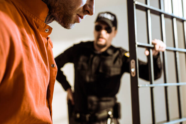 cropped image of prison guard looking at criminal in prison cell